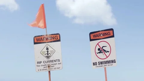 Rip current, no swimming beach warning signs, red flag blowing in wind. Stock Footage 133823638
