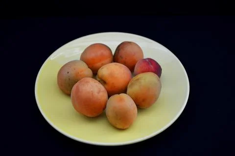 Ripe apricot fruit on a yellow plate on a black background Stock Photos