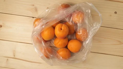 Ripe apricots in a plastic bag rotating on a wooden table Stock Footage 340526054
