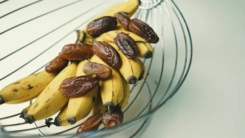 Ripe Bananas and Dates in Wire Basket, A wire fruit basket containing ripe .. Video stock 304974926