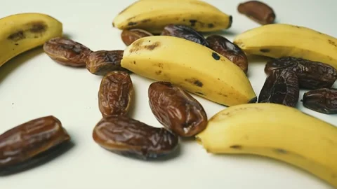Ripe Bananas and Dried Dates on White Surface, A close-up of ripe bananas a.. Видео 304975196