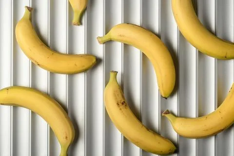 Ripe bananas create playful pattern on white ridged background with copy spac Stock Photos