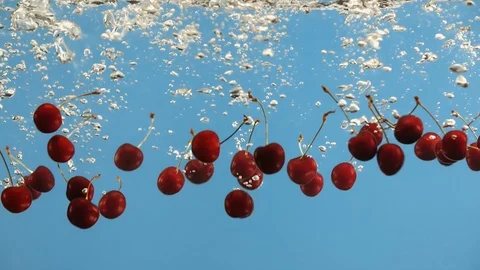 Ripe cherry fall into water on blue background. Red cherries berries in liquid Vídeo Stock 91014183