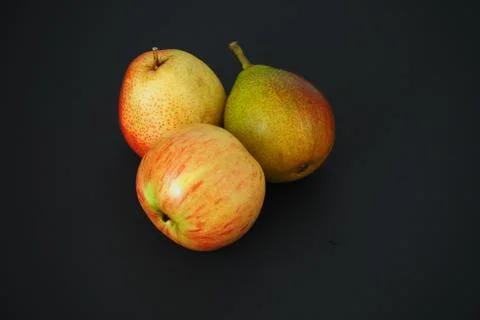 Ripe fruit on a black background. Two beautiful pears and an apple. Foto stock