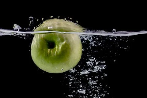 Ripe green apple falling down into clear water with splashes against black Stock Photos