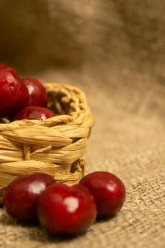 Ripe juicy cherries in a wicker basket and cherries scattered on a homespun f Stock Photos