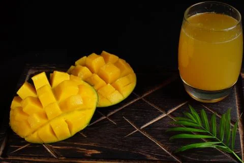 Ripe mango and juice in a glass on a wooden board with palm leaf Stock Photos