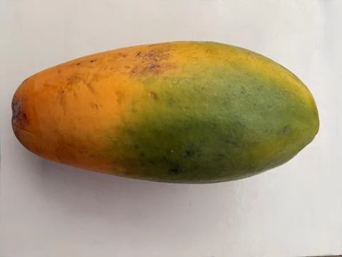 A ripe mango features both yellow and green hues, displayed on a white surfac Фото
