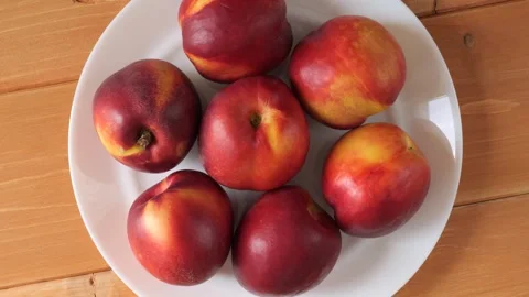 Ripe nectarines rotating on a plate over a wooden background Stock Footage 343435585