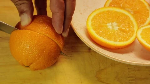 Ripe orange being cut in half on a wooden board, with fresh slices alongside 스톡 동영상 338337160