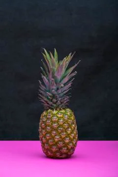 Ripe pineapple fruit on a pink table on a dark background Stock Photos