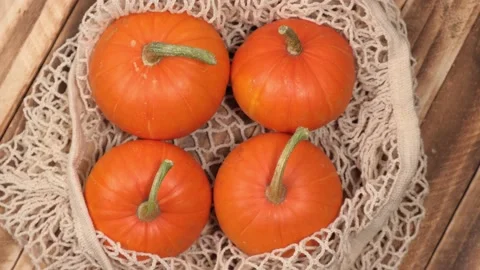 Ripe pumpkins in a string bag rotate on a wooden background. top view. closeup. Stock Footage 232444450