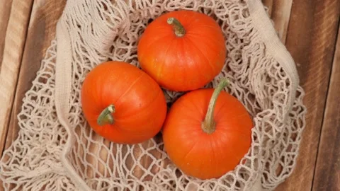 Ripe pumpkins in string bag, rotating on wooden background. top view. 4k. Stock Footage 219323235