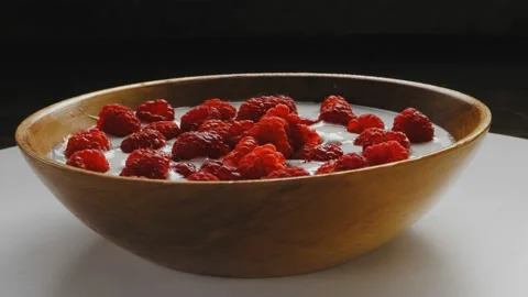Ripe raspberries float in thick cream in a wooden bowl. Rotate in a circle Stock Footage 203846275