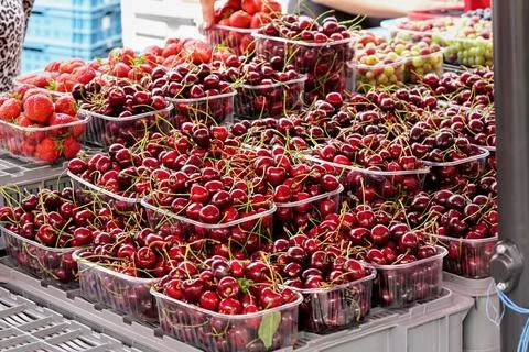 Ripe red cherries in plastic boxes on display at street food market, blurred  Stock Photos