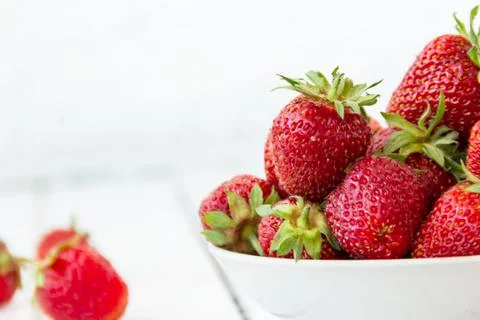 Ripe red strawberries lie in a white cup on a wooden white table. Copy space Stock Photos