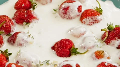 Ripe strawberries with green sprigs fall into the cream in a slow motion plate 库存影片 201475899