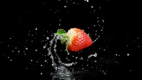 Ripe Strawberry Falling Down, Splashing Water and Spinning in the Air Stock Footage 107994352