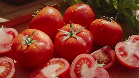 Ripe tomatoes and cut tomatoes on a sunlit wooden table with greenery. Stock Footage 345505003