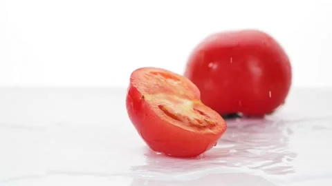 A ripe tomatoes are falling on the white table, splashing water drops. Stock Footage 147380032