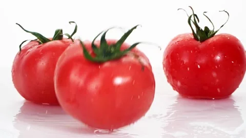 A ripe tomatoes are falling on the white table, splashing water drops. Stock Footage 147380033