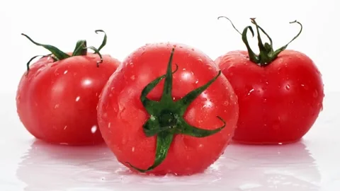 A ripe tomatoes are falling on the white table, splashing water drops. Stock Footage 147380034