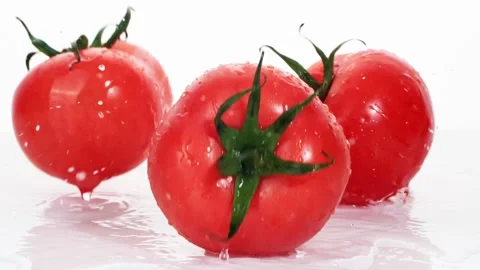 A ripe tomatoes are falling on the white table, splashing water drops. Stock Footage 147380037