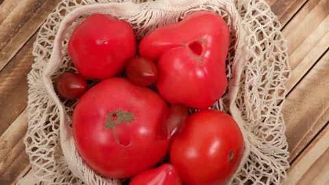 Ripe tomatoes in a string bag rotate on a wooden background. top view. closeup. Video stock 252446806