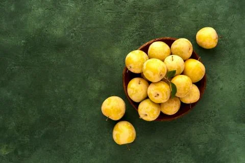 Ripe yellow plums in a wooden plate on green background. Top view with copy s Stock Photos