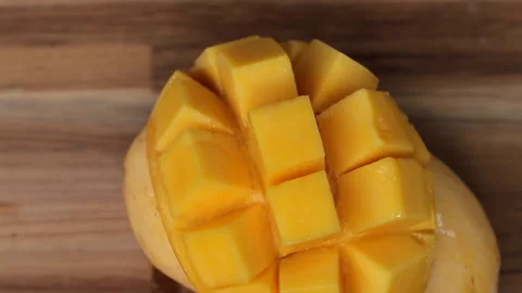 Ripped mango slice cubes cut rotating on a wooden background Stock Footage 274250757