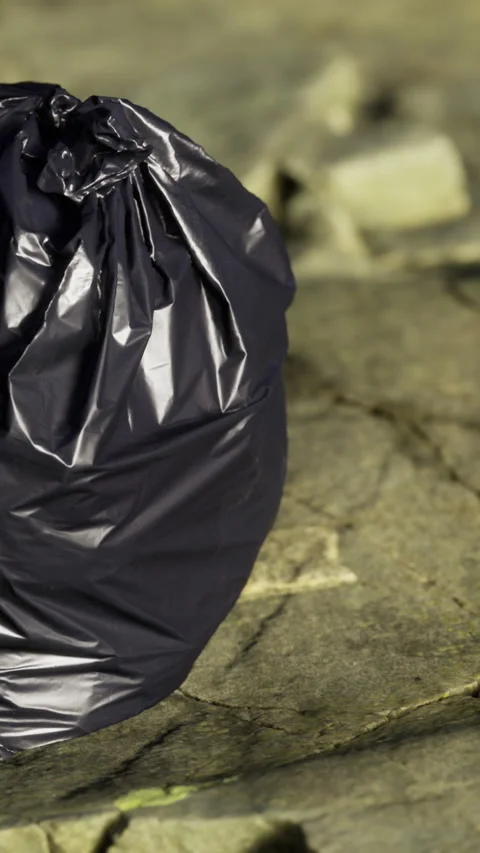 Ripped trash bag left on ground near pebble pathway during daylight hours Stock Footage 334882430