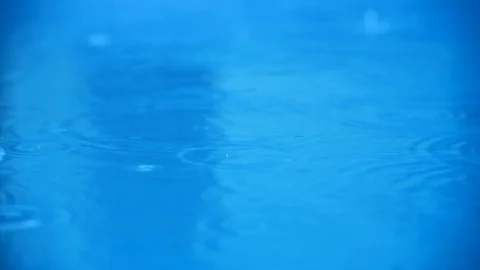 Rippled rain drops falling in blue water Stock Footage 112747892