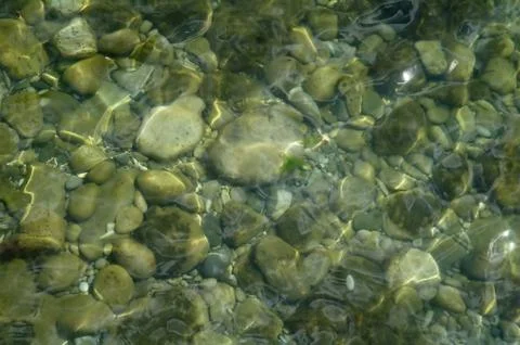 Ripples creating shadows onto round pebbles in water Stock Photos