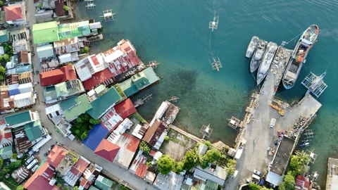 A riser tilt-down shot reveals Liminangcong Port with a cargo ship unloading 스톡 동영상 336692813
