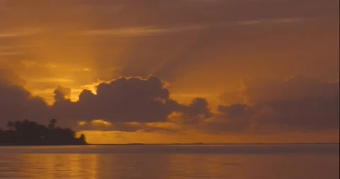 Rising sun behind clouds creating orange sky over the Moorea island ocean Stock Footage 138895017