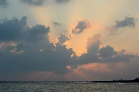 The rising sun hidden behind clouds above the ocean. Stock Photos