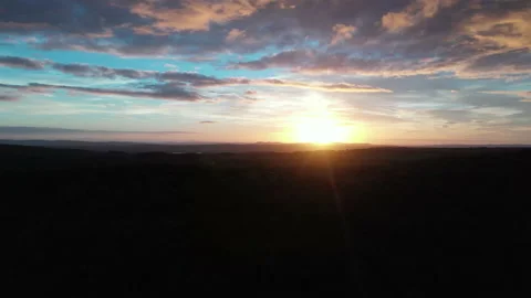 Rising view over silhouetted hill with sunrise revealed through moving clouds Stock Footage 231354331