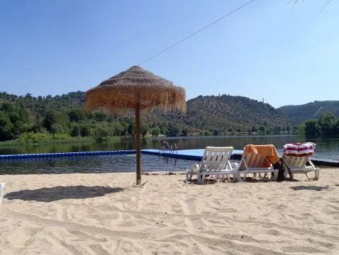 River beach with blue sky deck chairs sand and sun umbrella Stock Photos