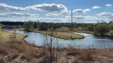 River bend in marshy meadow with power line pylon and blue cloudy sky Stock Footage 333510855