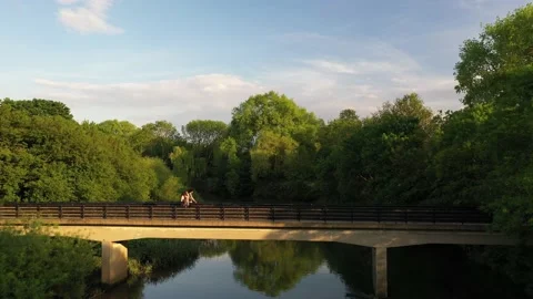 River calmly flowing through park, people walking on footbridge Stock Footage 156693318