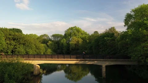 River calmly flowing through park, couple standing on footbridge Video stock 156693609