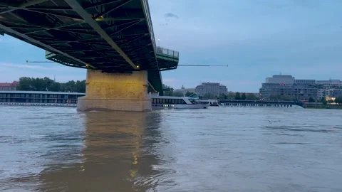 A river cruise ship glides under a modern bridge at dusk Vidéo 301279971