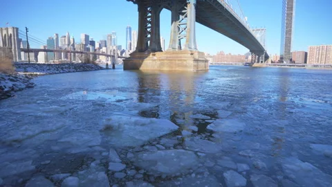 River edge under Manhattan Bridge is partially frozen in the morning at Brooklyn Vídeos de archivo 336826868