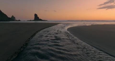 River estuary flowing over the sand into the ocean at sunset. Anawhata, Piha, Stock Footage 280306722