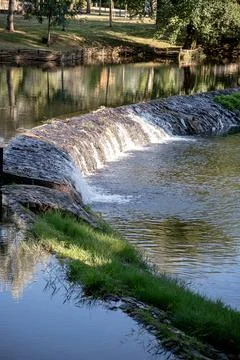 A river featuring a small stone dam with water cascading over the edge Stock Photos