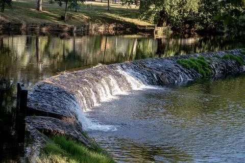 A river featuring a small stone dam with water cascading over the edge Stock Photos