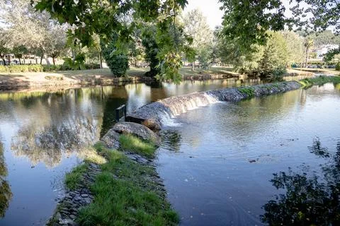 A river featuring a small stone dam with water cascading over the edge Stock Photos