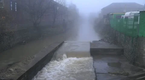 River flowing rapidly through town, man walks his dog on tow path in fog Stock Footage 15092911