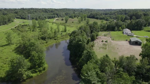 River flowing through hilly forest next to farm Video stock 272451767