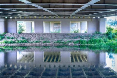 River flowing under bridge with perspective view of concrete columns and shor Stock Photos